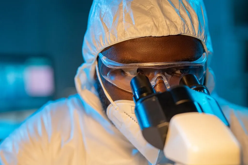 black microbiologist in ppe looking into microscope
